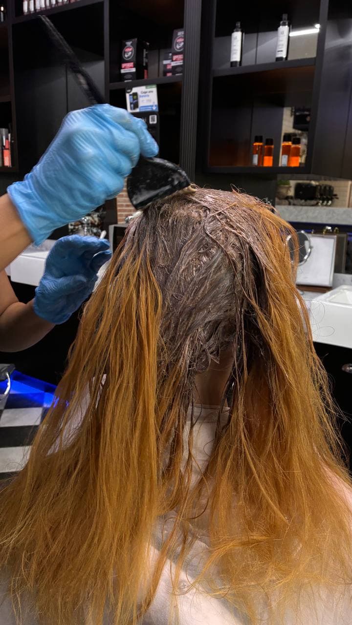 Colourist applying colour to the roots of orange lengths during a colour correction